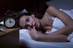 Insomnia patient awake in a bed with a table clock beside the bed